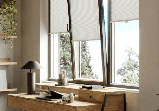 This image shows white clic honeycomb blinds fitted onto a black frame tilt and turn window, above a wooden desk.