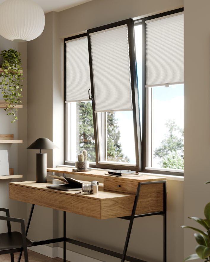 This image shows white clic honeycomb blinds fitted onto a black frame tilt and turn window, above a wooden desk.