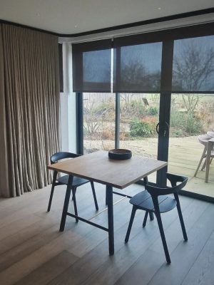 This image shows black semi-transparent roller blinds, fitted onto large sliding doors looking out onto a garden with decking.