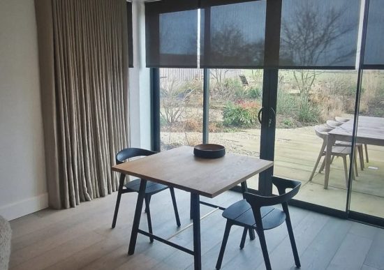 Roller Blinds This image shows black semi-transparent roller blinds, fitted onto large sliding doors looking out onto a garden with decking.