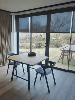 This image shows black semi-transparent roller blinds, fitted onto large sliding doors looking out onto a garden with decking.
