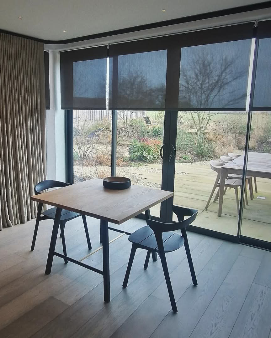 This image shows black semi-transparent roller blinds, fitted onto large sliding doors looking out onto a garden with decking.