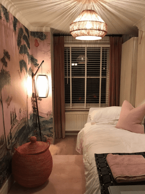 This image shows white Venetian blinds in a dimly lit room with a small bed and a Japanese mural painted on the wall.