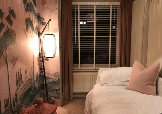 Venetian blinds This image shows white Venetian blinds in a dimly lit room with a small bed and a Japanese mural painted on the wall.
