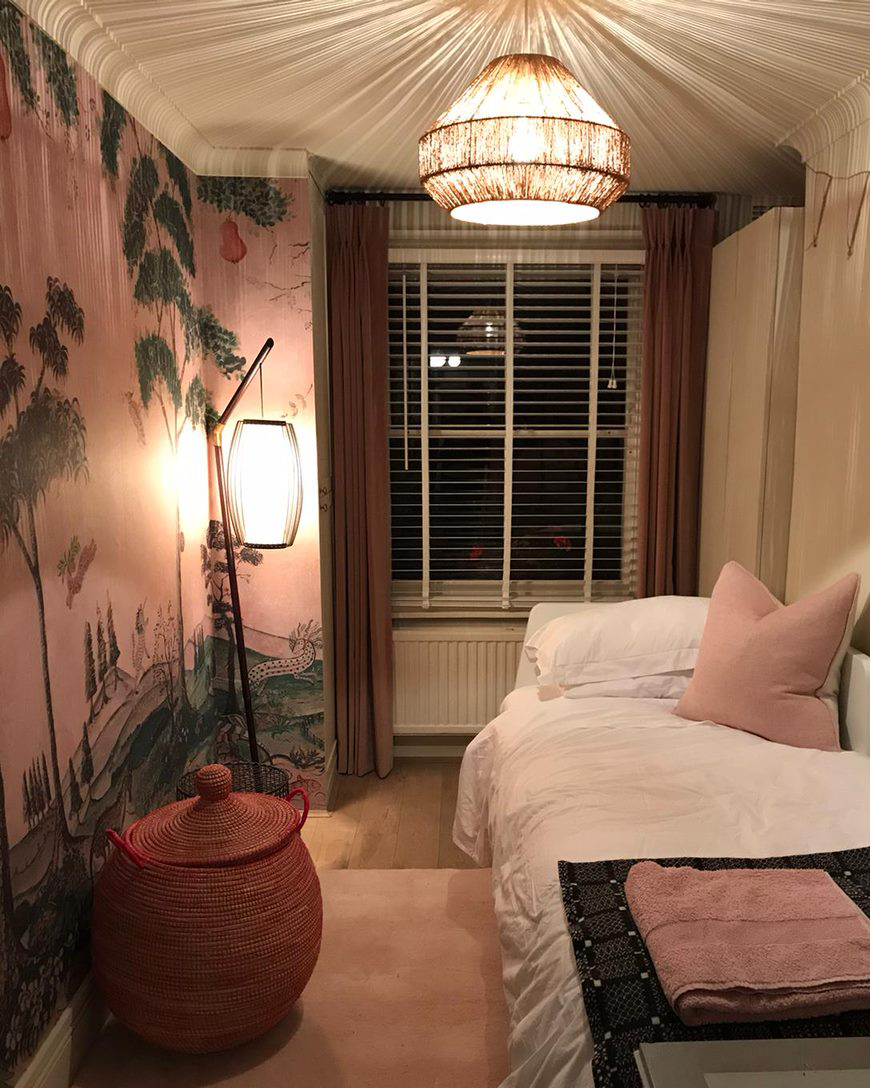 This image shows white Venetian blinds in a dimly lit room with a small bed and a Japanese mural painted on the wall.