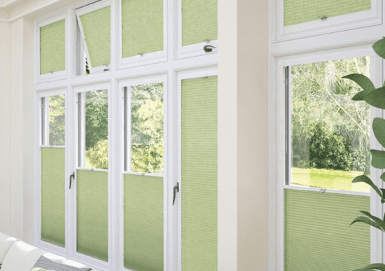 This image shows light green perfect-fit blinds attached to white window frames. SOme are open and some are closed.