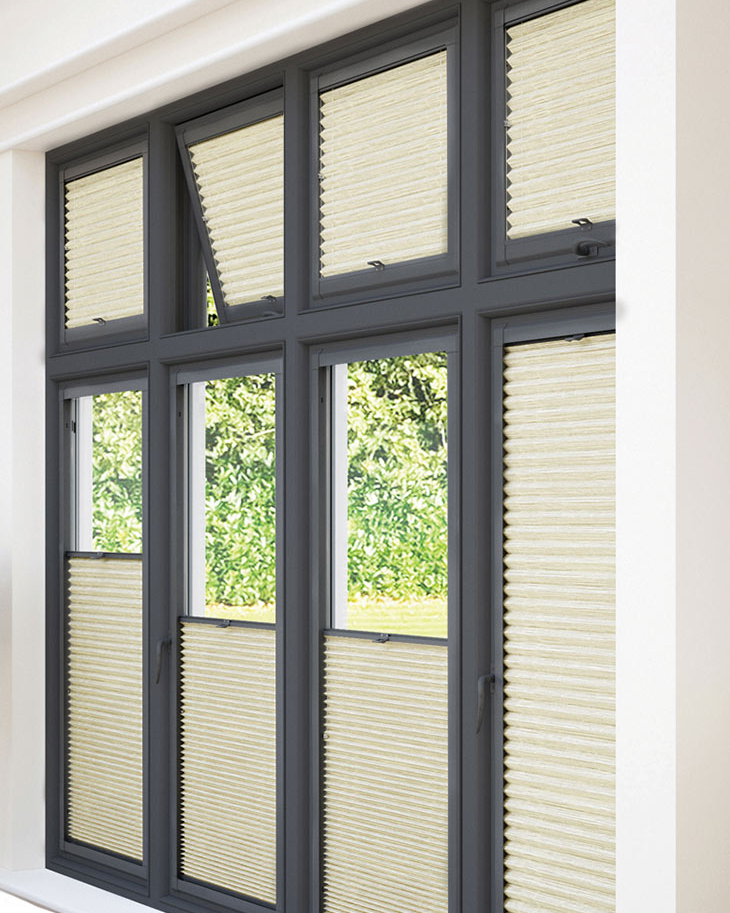 This image shows sand coloured perfect-fit honeycomb blinds, half up and half down, fitted onto black window frames.