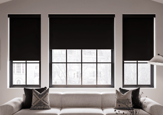 A picture of blackout blinds, which are half rolled up on three living room windows.